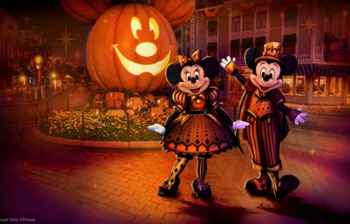 Mickey and Minnie Mouse in their Halloween garb in front of a large Mickey jack-o-lantern at Disneyland