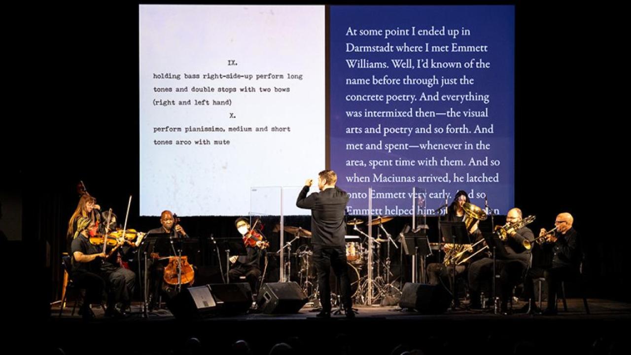 Orchestra with text displayed on a screen behind it