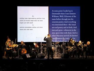 Orchestra with text displayed on a screen behind it